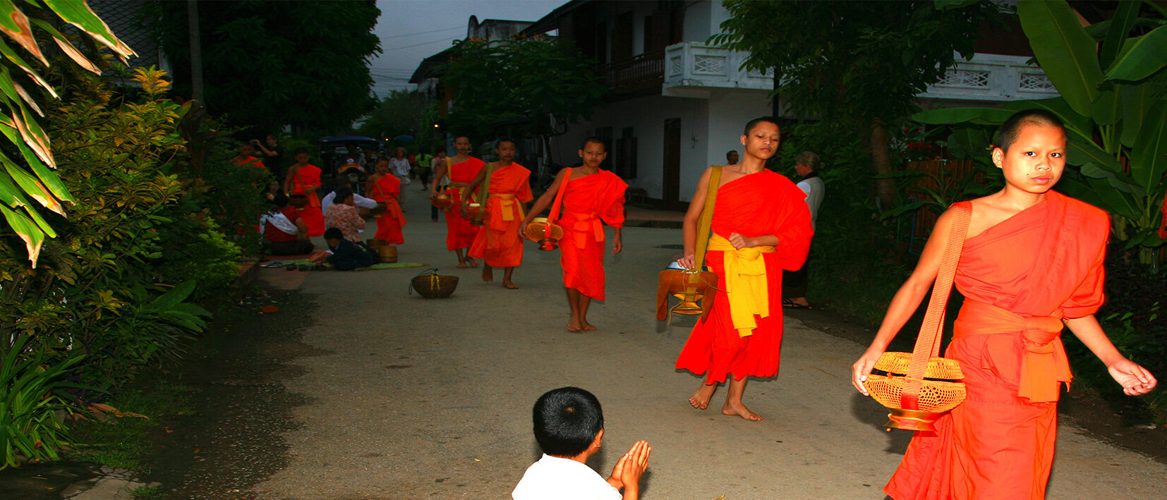 Jeunes moines assistant à la cérémonie matinale du Tak Bat à Luang Prabang lors d'un voyage au Laos sur mesure avec une agence locale Nirvatravel